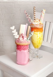 Tasty milk shakes with sweets in glassware on chair near brick wall