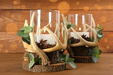 Photo of Stylish holders with burning candles, coffee beans and eucalyptus on wooden table
