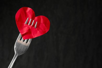 Photo of Broken heart. Red paper heart pierced with fork against black background, closeup. Space for text