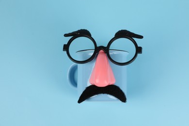 Photo of Man's face made of cup, fake mustache, nose and glasses on light blue background, top view