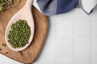 Photo of Wooden spoon with mung beans and board on white tiled table, flat lay. Space for text