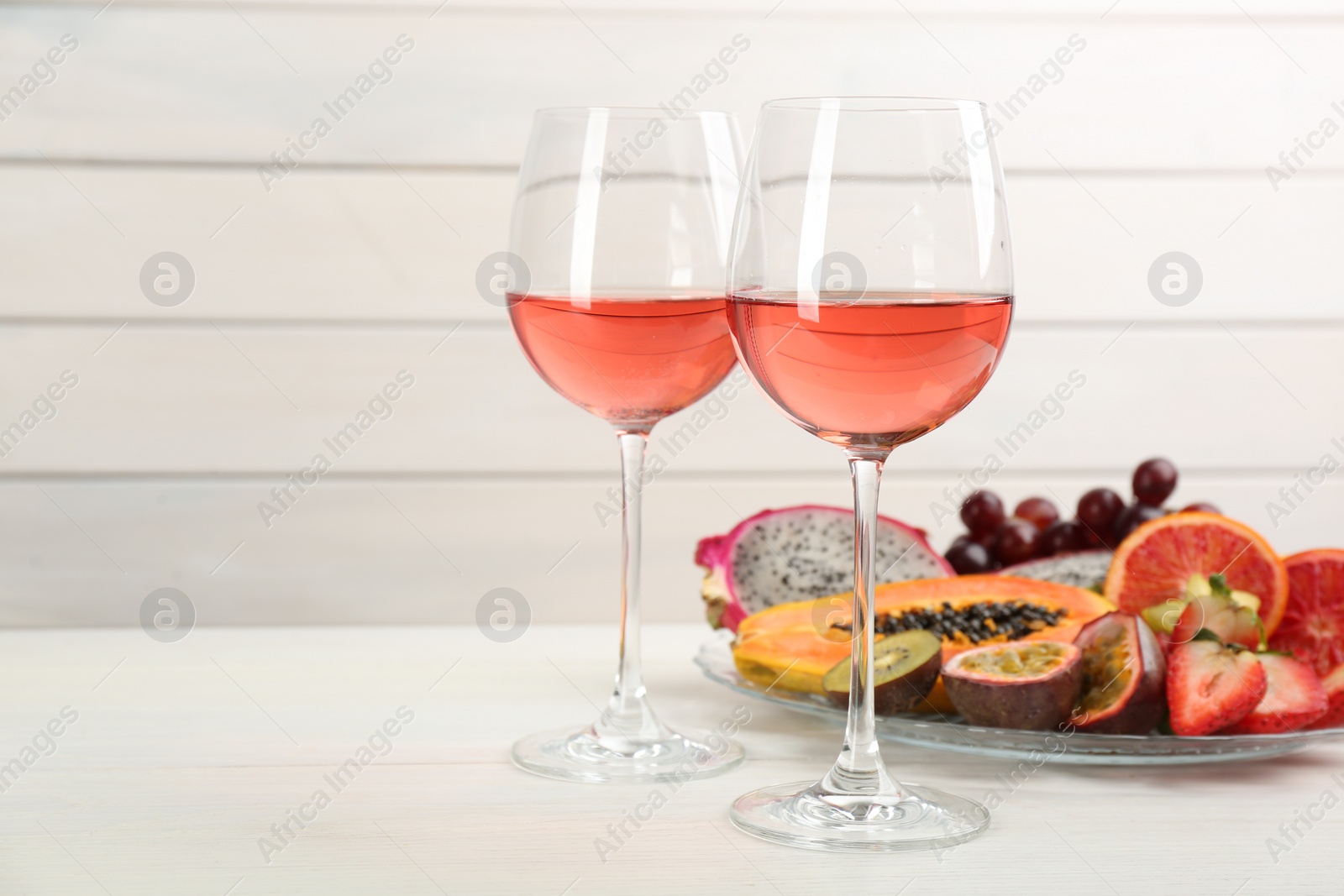 Photo of Delicious exotic fruits and wine on white wooden table. Space for text