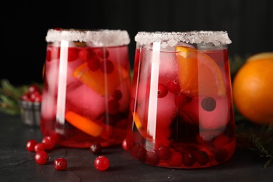 Photo of Tasty cranberry cocktail with ice cubes in glasses on dark gray textured table, closeup