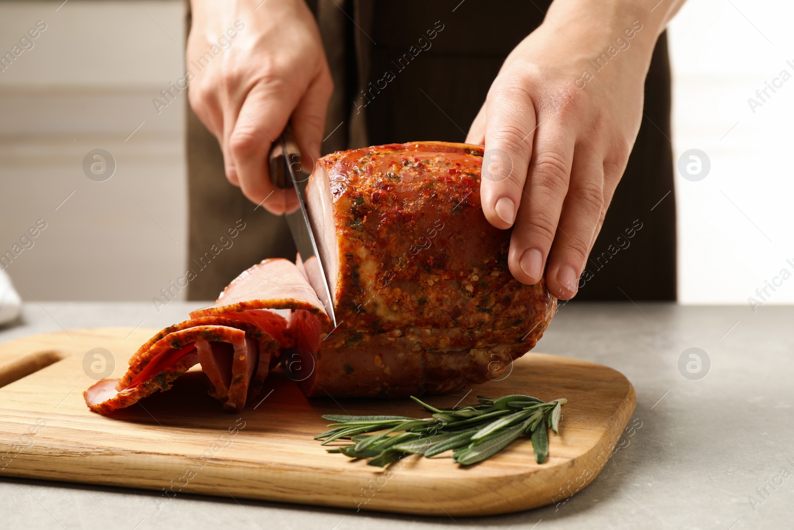 Photo of Woman cutting ham on wooden board at table, closeup