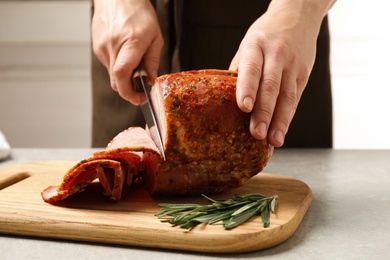 Photo of Woman cutting ham on wooden board at table, closeup