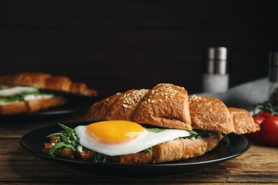 Delicious croissant with arugula and fried egg on wooden table