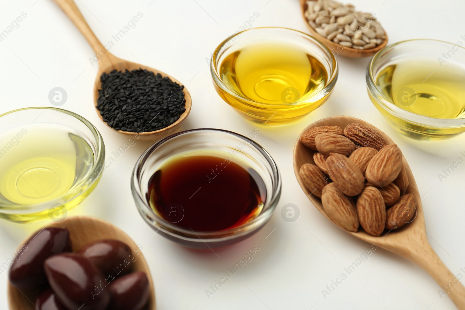 Photo of Vegetable fats. Different cooking oils in bowls and spoons with ingredients on white background, closeup