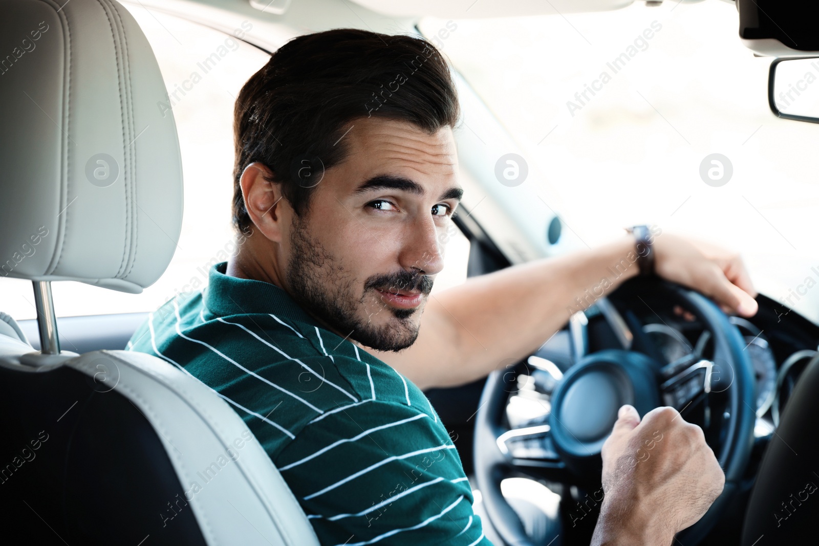 Photo of Attractive young man driving luxury car, view from backseat