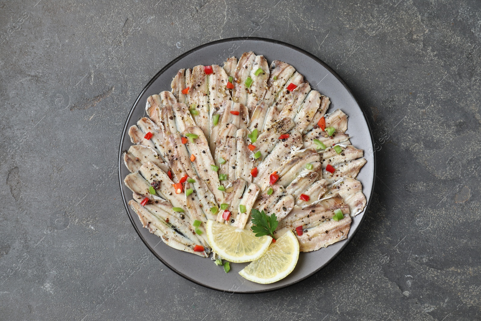 Photo of Tasty pickled anchovies with spices on grey textured table, top view