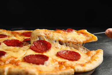 Photo of Taking slice of tasty pepperoni pizza on black table, closeup