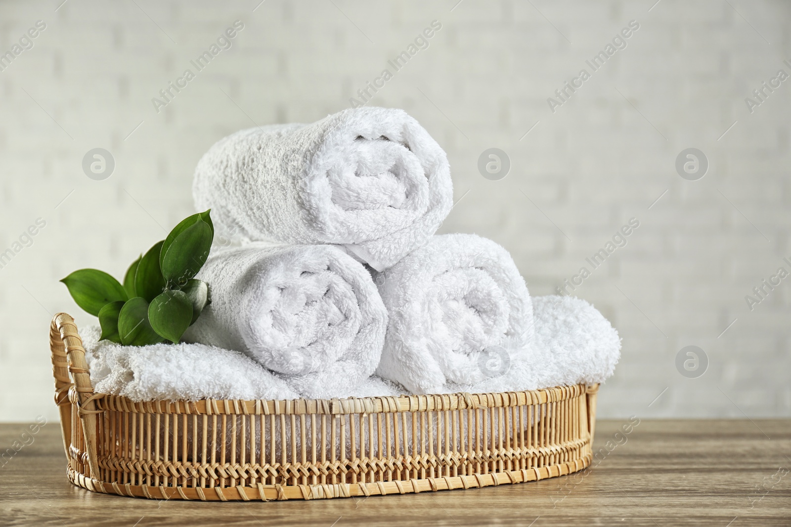 Photo of Wicker basket with rolled bath towels and green branch on wooden table