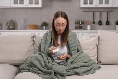 Young woman pouring antidepressants from bottle on sofa at home