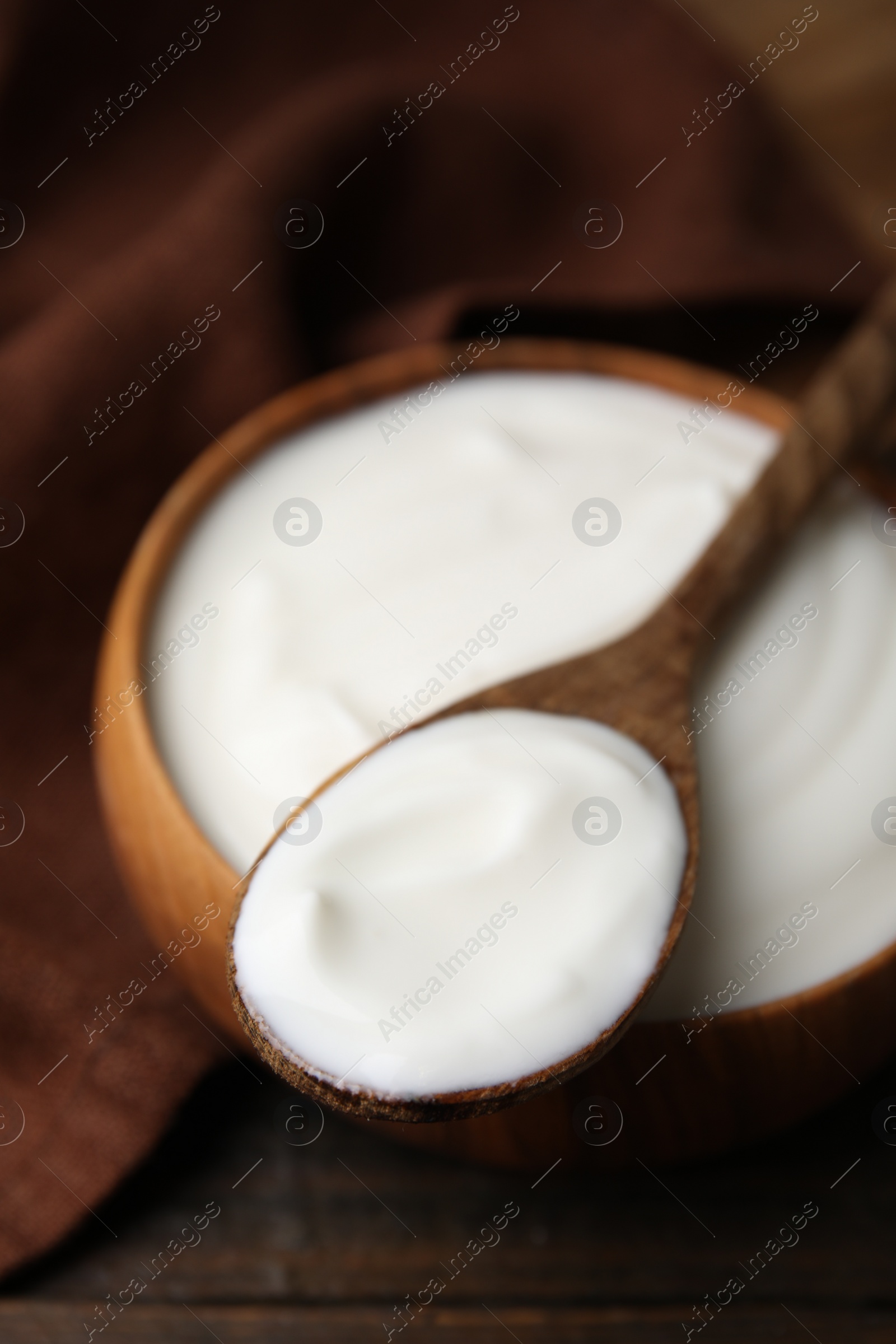 Photo of Delicious natural yogurt in bowl and spoon on wooden table, closeup