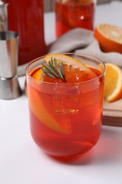Aperol spritz cocktail, ice cubes, rosemary and orange slices in glass on white wooden table, closeup