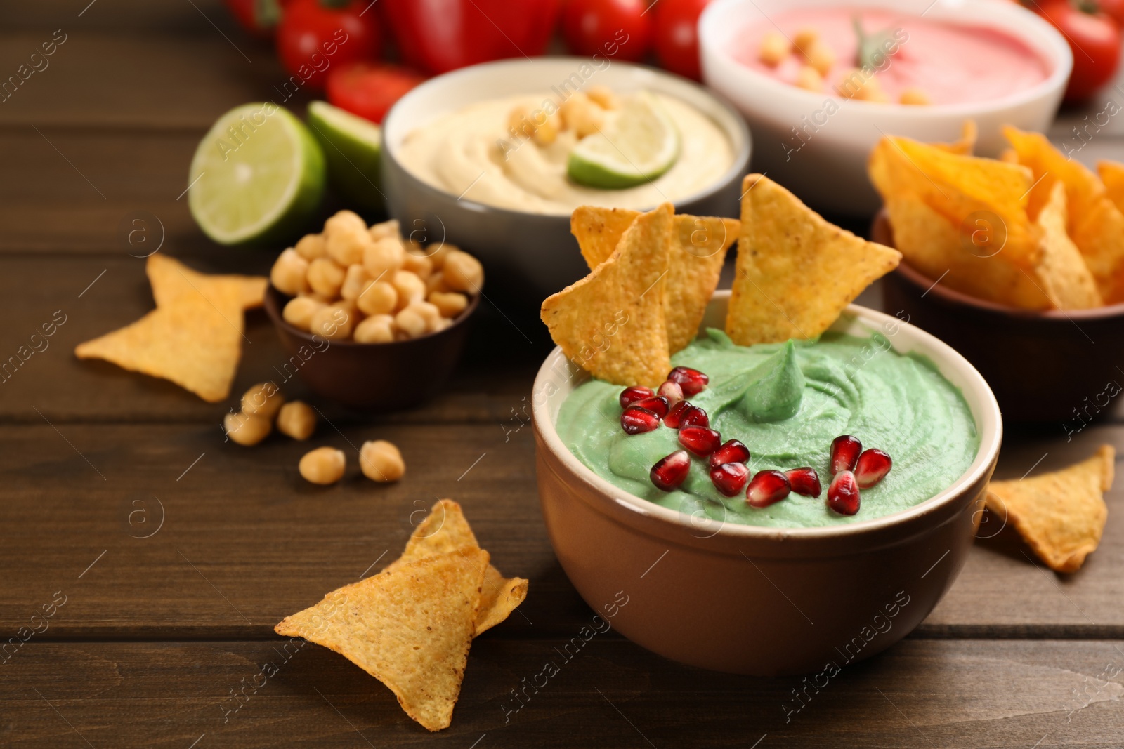 Photo of Different kinds of tasty hummus, nachos and ingredients on wooden table