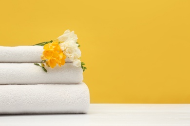 Photo of Stack of soft clean towels with beautiful flowers on table against color background. Space for text