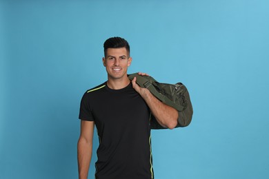 Handsome man with sports bag on light blue background