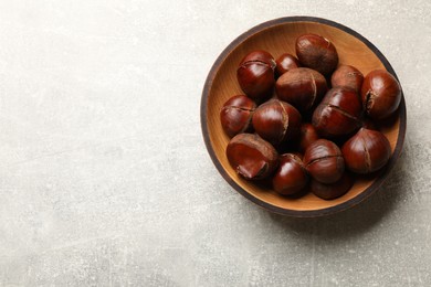 Fresh edible sweet chestnuts in wooden bowl on grey table, top view. Space for text