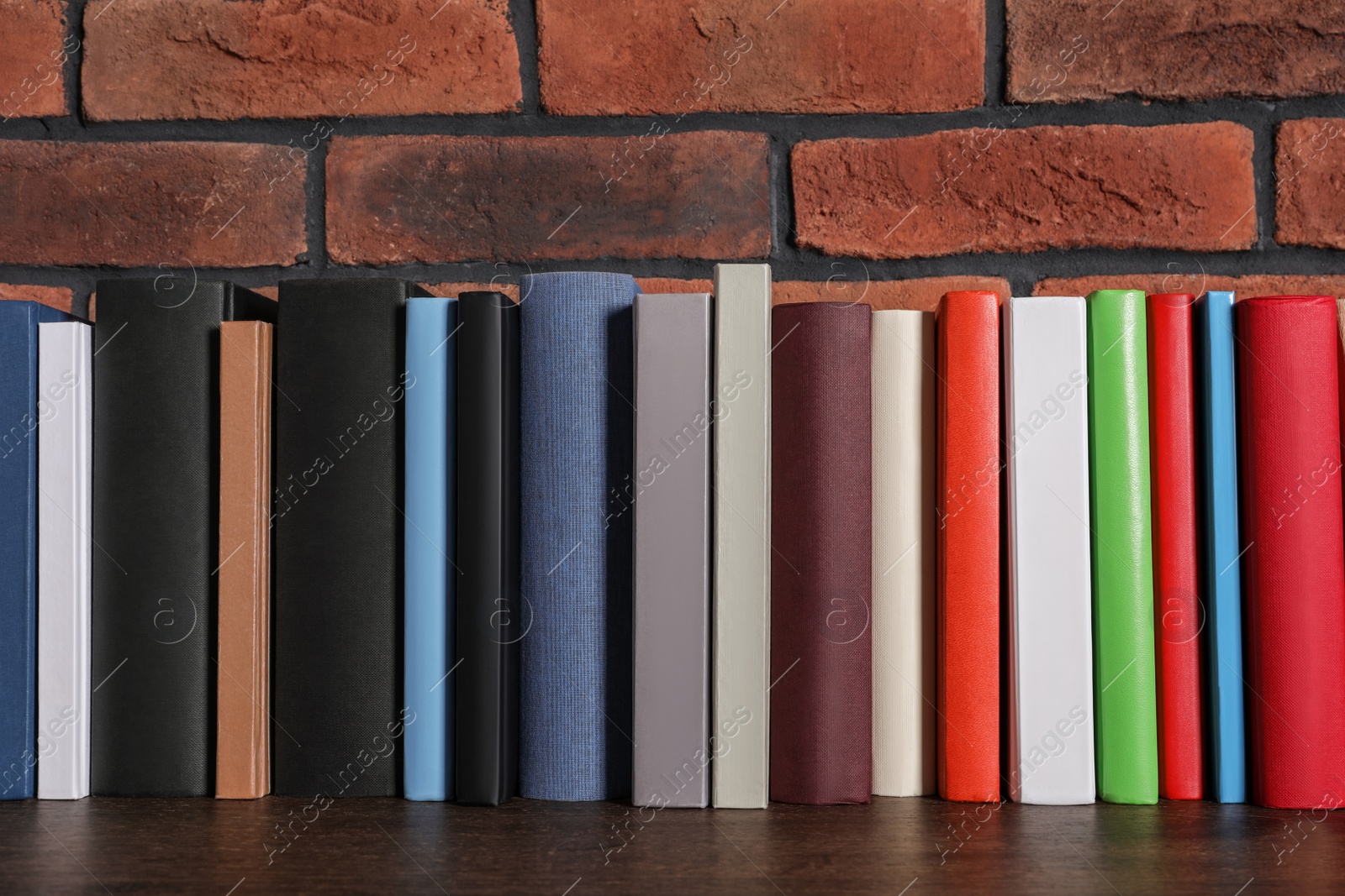 Photo of Many hardcover books on wooden table near brick wall