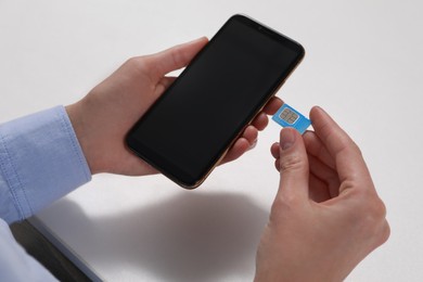 Woman with SIM card and smartphone at white table, closeup
