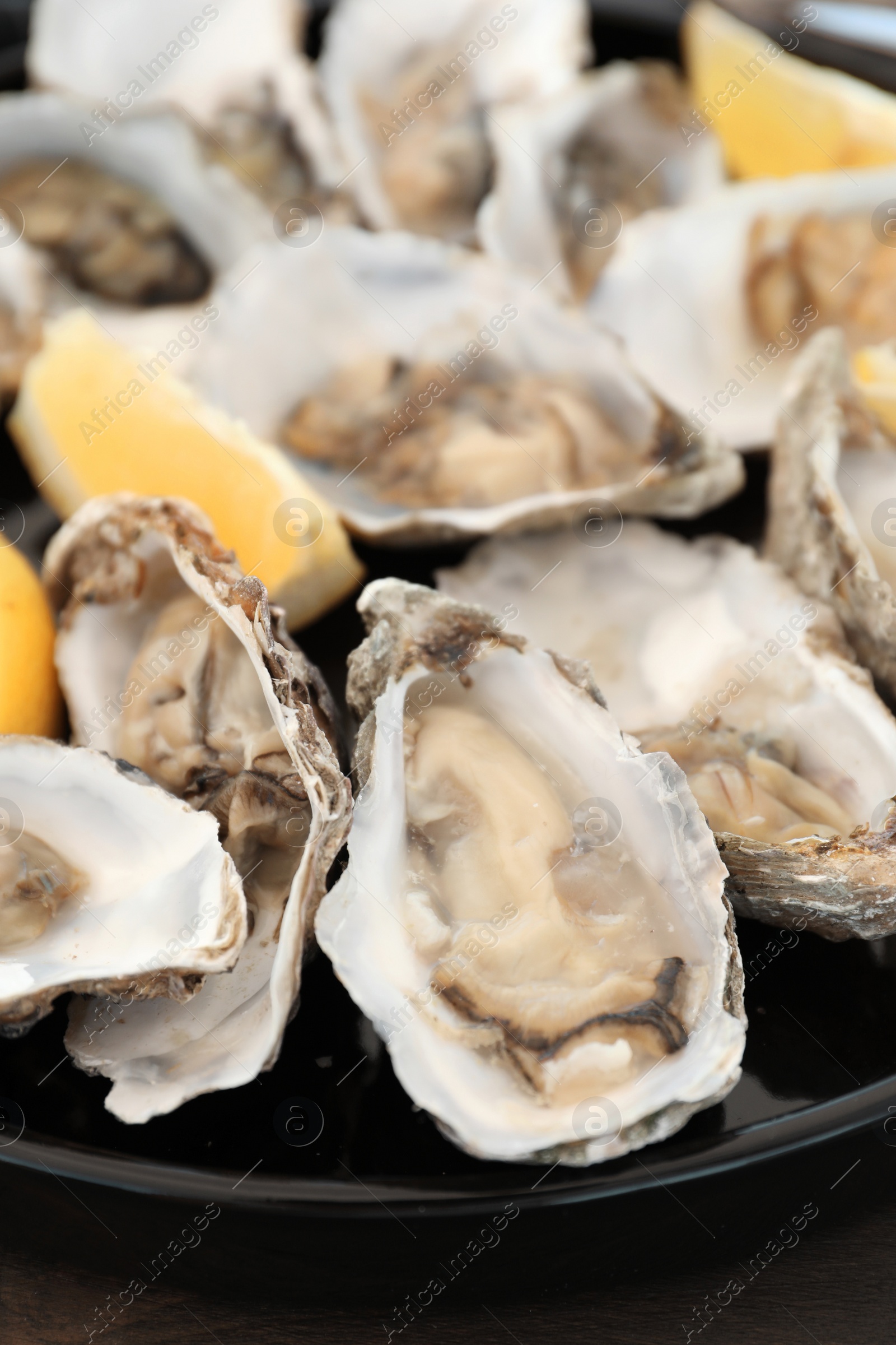 Photo of Fresh oysters with cut juicy lemon on plate, closeup