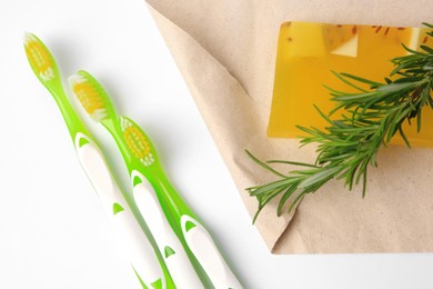 Light green toothbrushes, solid soap and rosemary on white background, top view