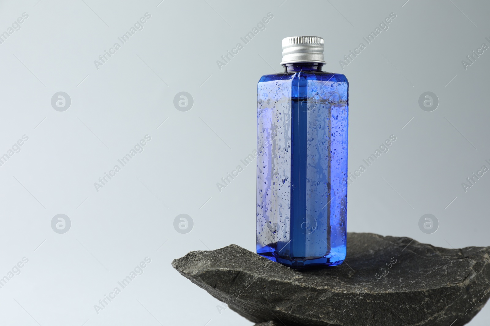 Photo of Bottle of cosmetic product on stone against light grey background, space for text