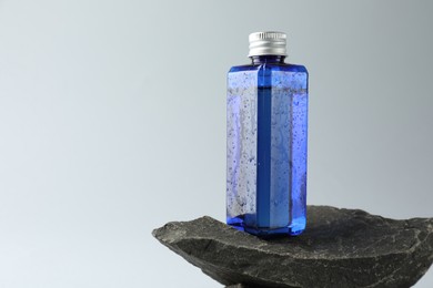 Bottle of cosmetic product on stone against light grey background, space for text