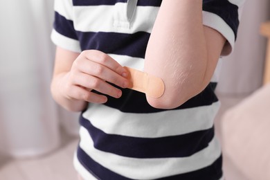 Little boy putting sticking plaster onto elbow indoors, closeup