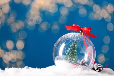 Photo of Decorative snow globe with red ribbon against blurred festive lights, closeup. Space for text