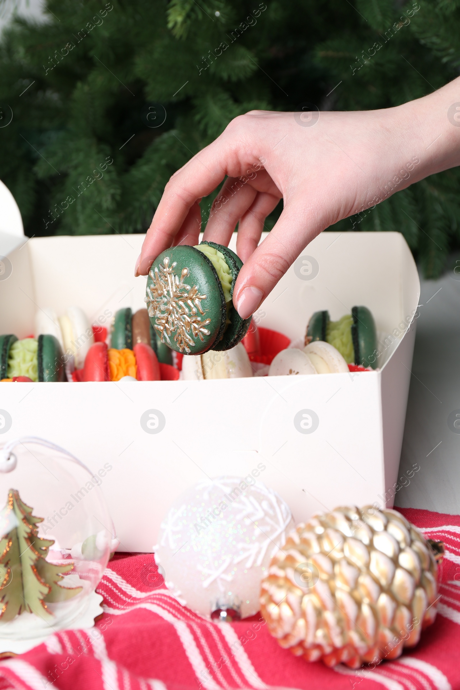 Photo of Woman with box of decorated Christmas macarons at table, closeup