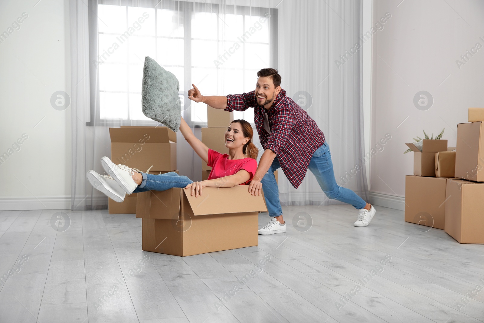 Photo of Happy couple playing with cardboard box in their new house. Moving day