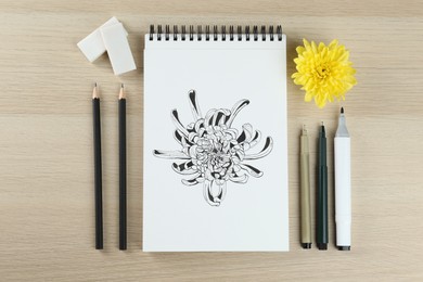 Drawing of chrysanthemum with flower and art supplies on wooden table, flat lay