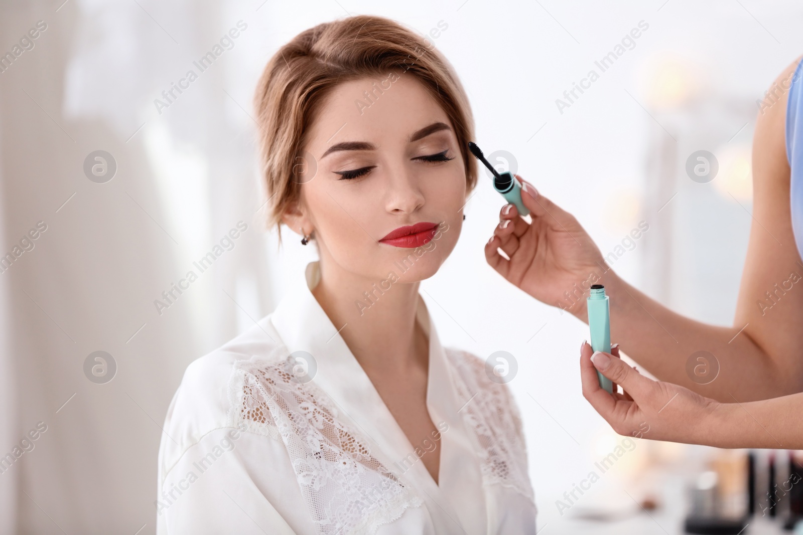Photo of Makeup artist preparing bride before her wedding in room
