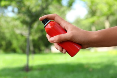 Woman with bottle of insect repellent spray outdoors, closeup