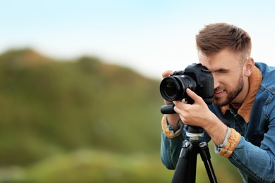 Male photographer taking picture of beautiful landscape with professional camera on green hill. Space for text