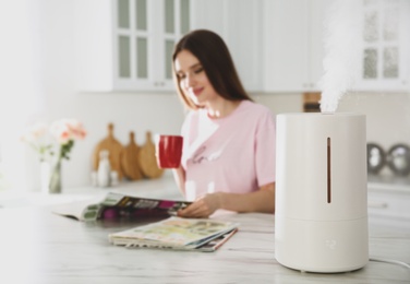 Photo of Modern air humidifier and blurred woman drinking coffee in kitchen