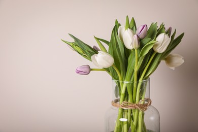 Photo of Beautiful bouquet of colorful tulips in glass vase on beige background. Space for text