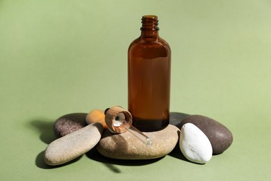 Photo of Bottle of face serum and dropper on spa stones against light green background