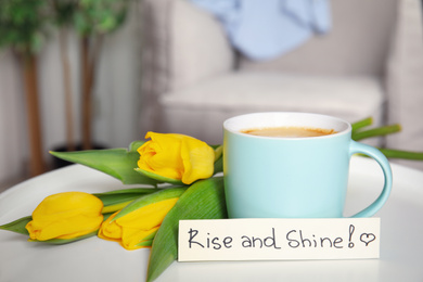 Photo of Aromatic morning coffee, beautiful flowers and card with RISE AND SHINE wish on white table indoors