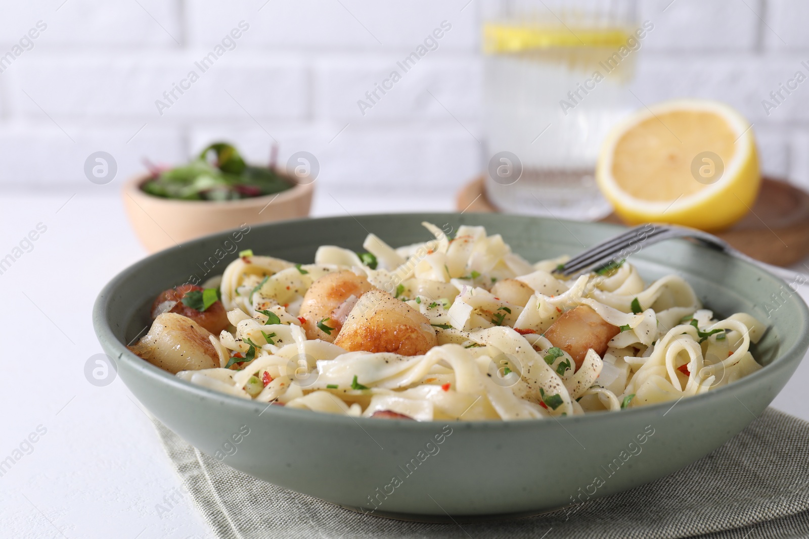 Photo of Delicious scallop pasta with spices in bowl served on white table, closeup