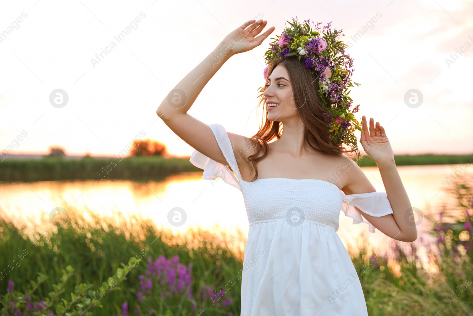 Photo of Young woman wearing wreath made of beautiful flowers outdoors at sunset