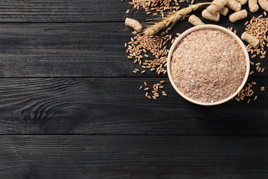 Photo of Bowl of wheat bran on black wooden table, flat lay. Space for text