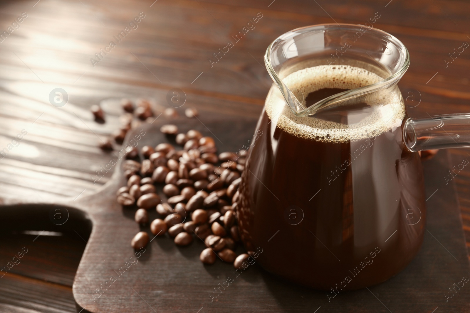 Photo of Glass turkish coffee pot with hot drink and beans on wooden table, space for text