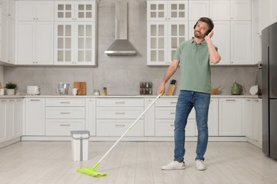 Photo of Enjoying cleaning. Man in headphones listening to music and mopping floor in kitchen