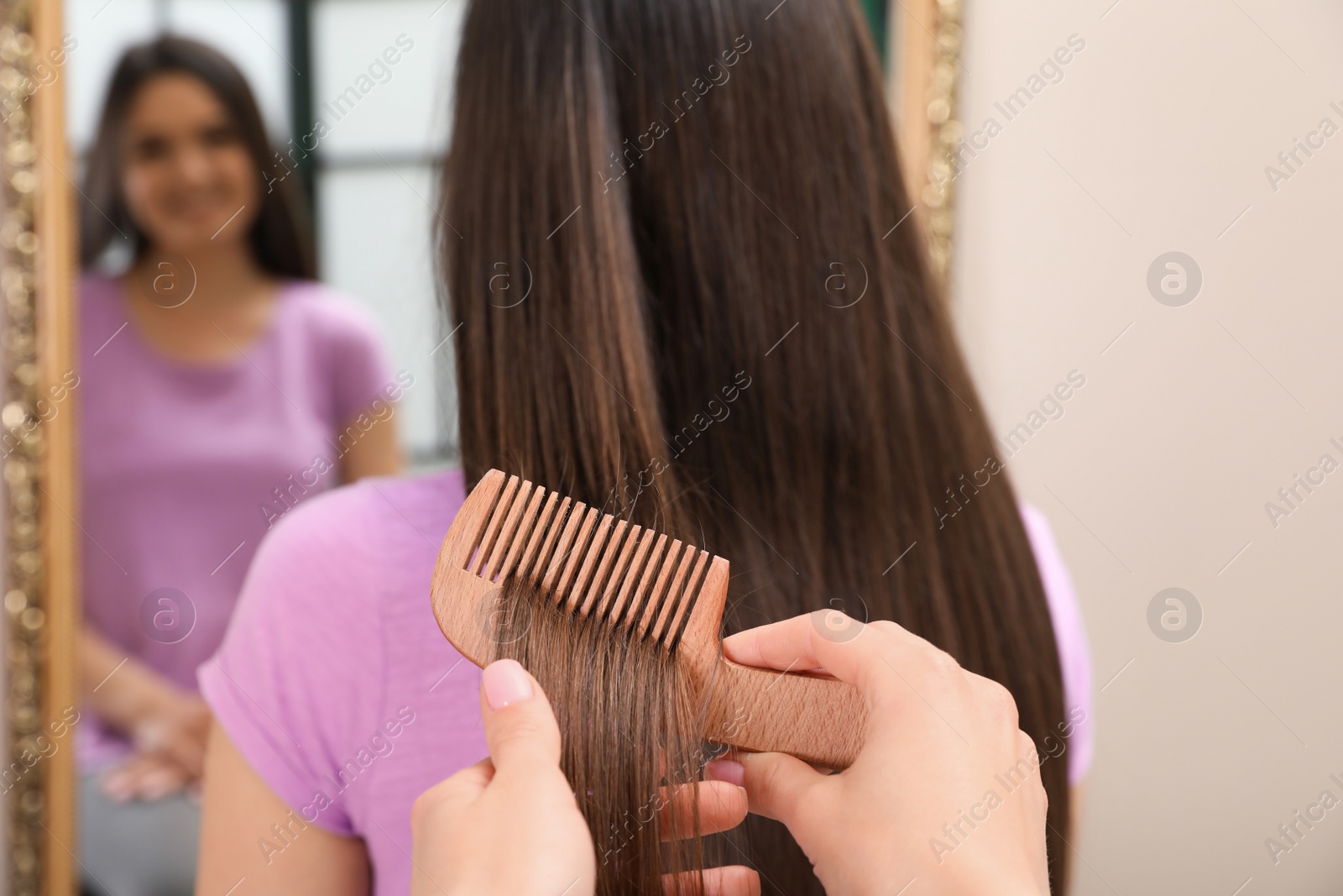 Photo of Woman combing friend's hair indoors, closeup view