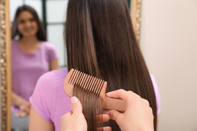 Woman combing friend's hair indoors, closeup view