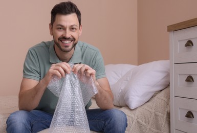 Photo of Man popping bubble wrap in bedroom at home. Stress relief