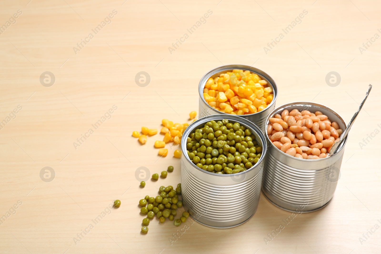 Photo of Open tin cans of conserved vegetables on wooden background, space for text