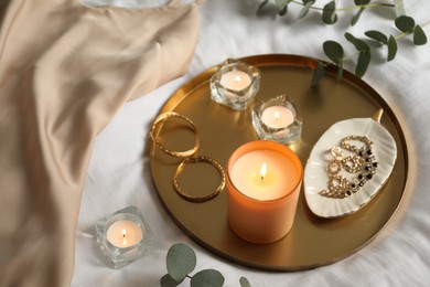 Tray with beautiful candles and jewelry on bed